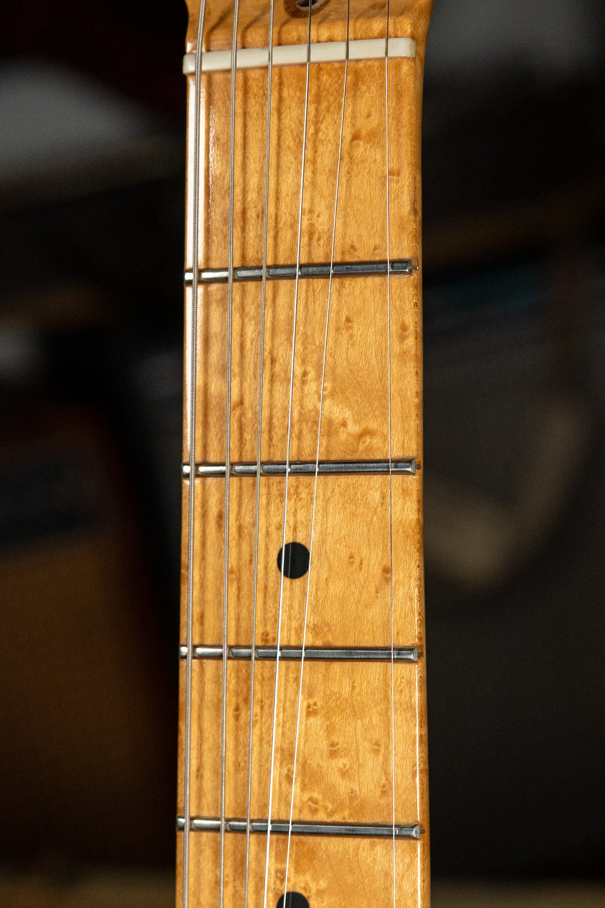 Close-up of the light brown maple fretboard with dark grain, showing a black dot inlay at the 7th fret and six strings.