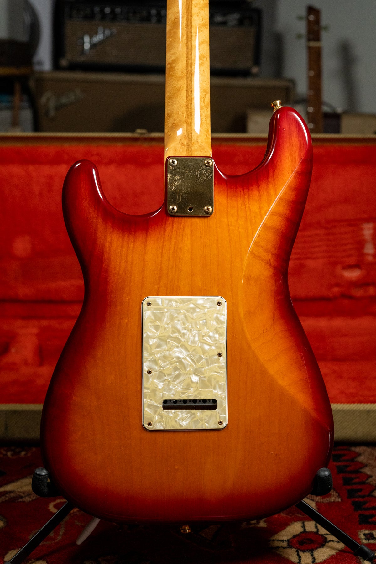 The back of a sunburst Stratocaster with a pearloid tremolo cover, a gold neck plate, and a figured maple neck.