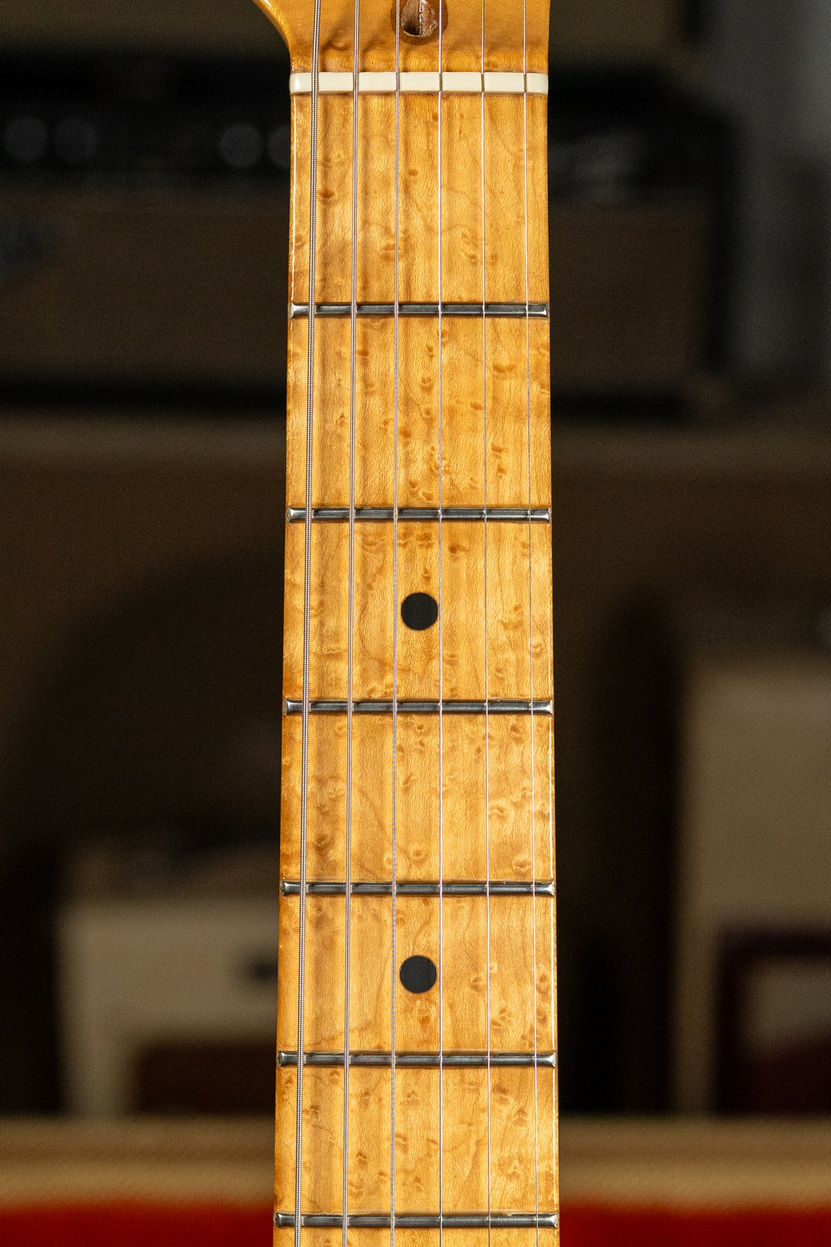 Close-up of the guitar's light-colored, highly figured maple fretboard with black dot inlays, showing frets and strings.