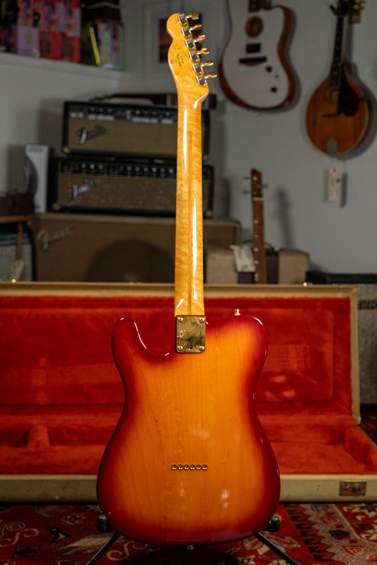 The back of a sunburst Telecaster with a flame maple neck and gold hardware, standing in its open red-lined case.