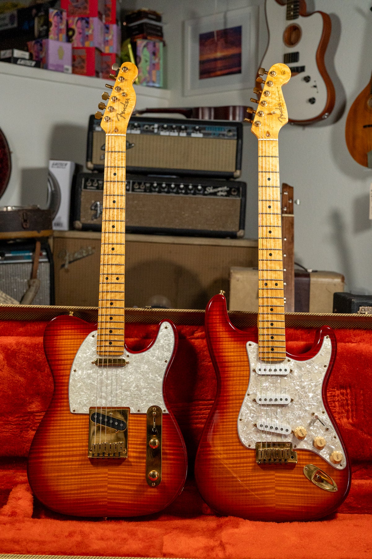 Two flame-top guitars, a Telecaster and a Stratocaster, with gold hardware and pearloid pickguards, rest in a red velvet case.