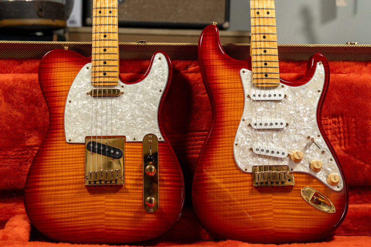 Two sunburst guitars with flame maple tops and pearloid pickguards rest in a red velvet case, showing minimal wear.