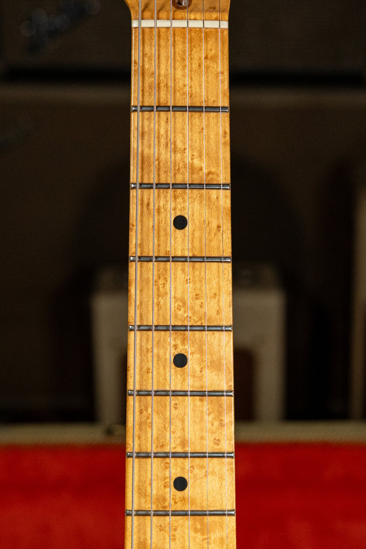 Close-up of the light brown maple fretboard with dark circular inlays, showing subtle birdseye figuring and light wear on the frets.