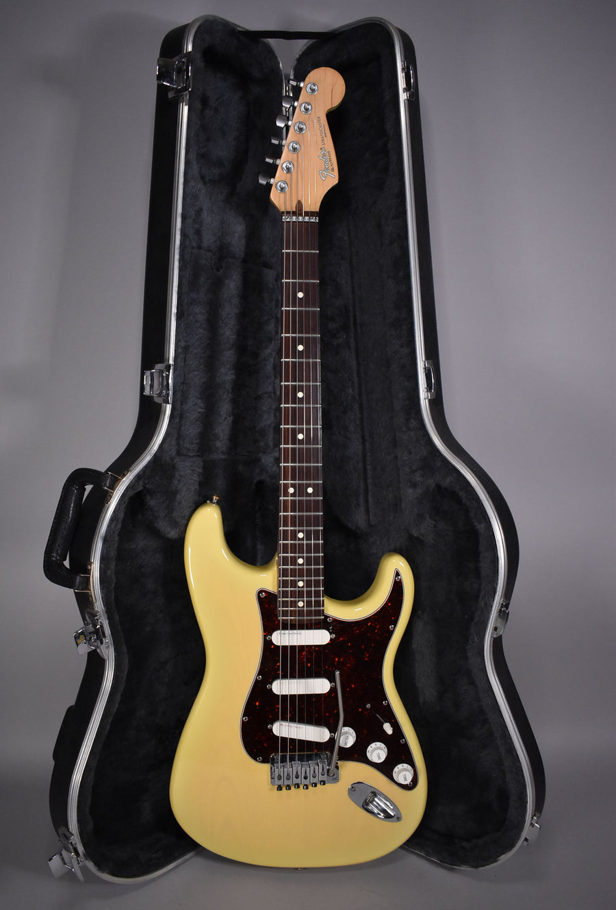 Full-length view of a vintage blonde Stratocaster with a tortoiseshell pickguard, white pickups, and chrome hardware, resting in its open hard case.