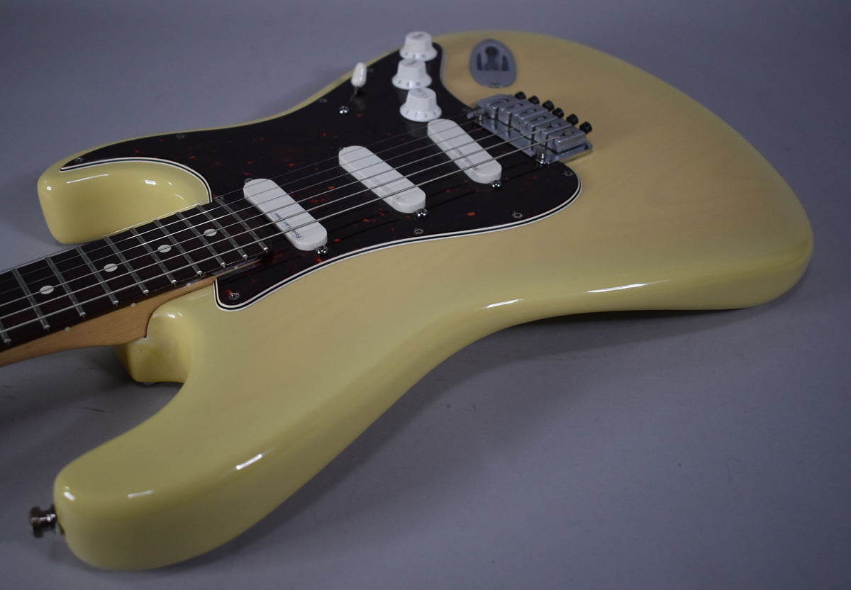 Vintage blonde Stratocaster body, angled from the lower bout, showing the black pickguard, three white single-coil pickups, and chrome bridge.