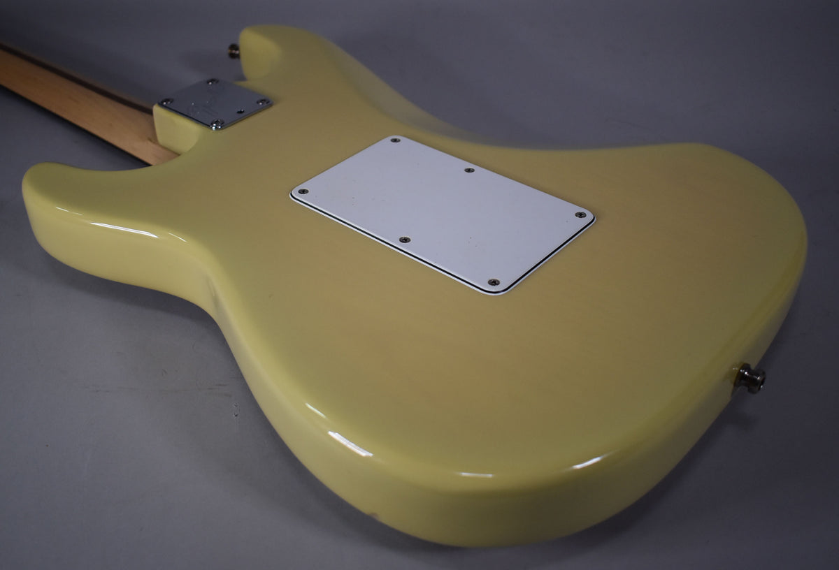 The back of a vintage blonde Stratocaster body, showing the white tremolo cover, chrome neck plate, and output jack.