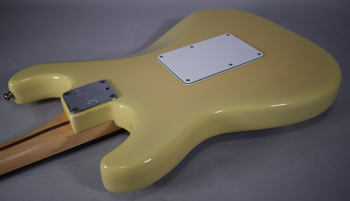 The back of a vintage blonde Stratocaster body, showing the neck plate, output jack, and white tremolo cover.