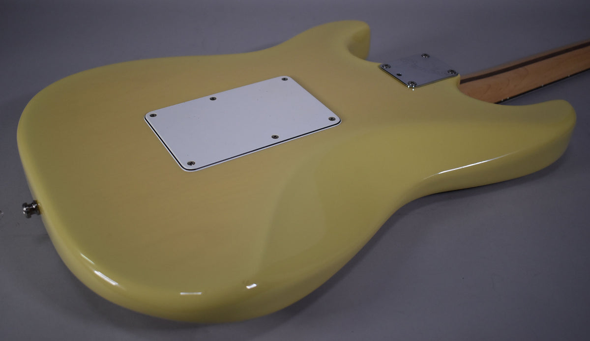 The vintage blonde Stratocaster body is viewed from the back, showing the white tremolo cavity cover and a chrome neck plate.