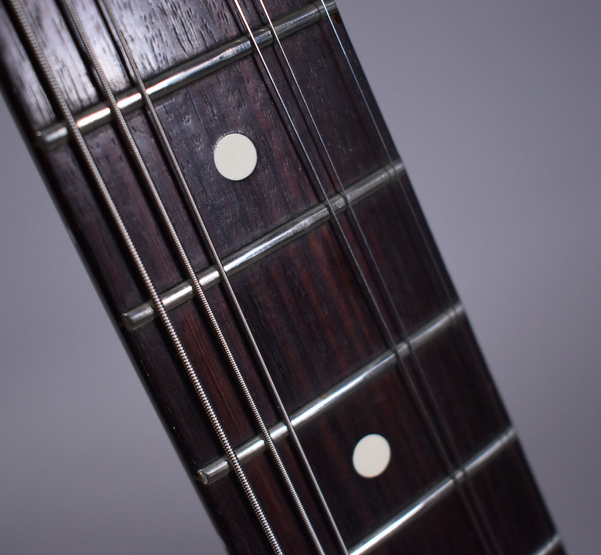 Close-up of the dark rosewood fretboard with white dot inlays, showing light wear on the frets and strings.