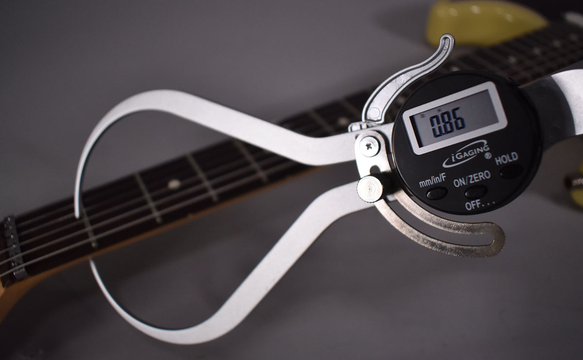 A digital caliper measures the fret height on the dark rosewood fretboard of the vintage blonde guitar.