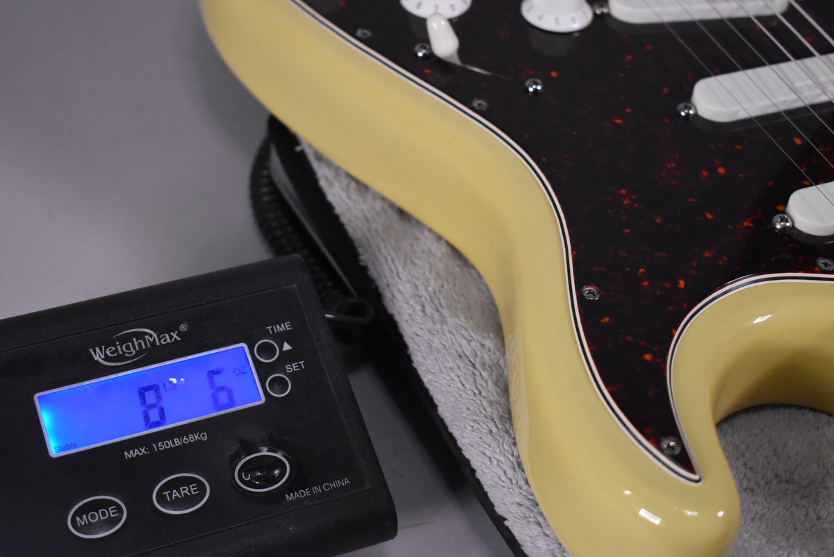 The vintage blonde Stratocaster body, with a tortoiseshell pickguard, rests on a scale displaying 8 lbs 6 oz.