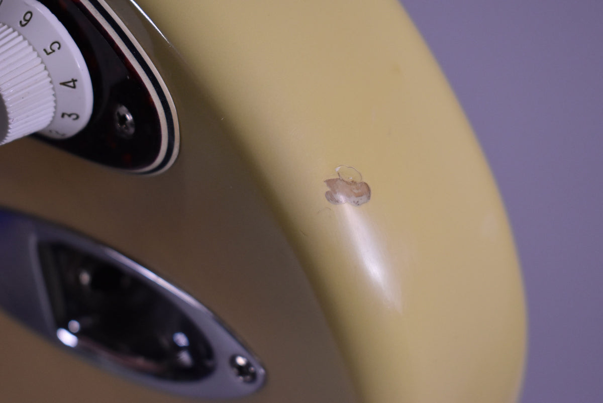 Close-up of the vintage blonde body, showing a large chip in the finish near the input jack and a white control knob.