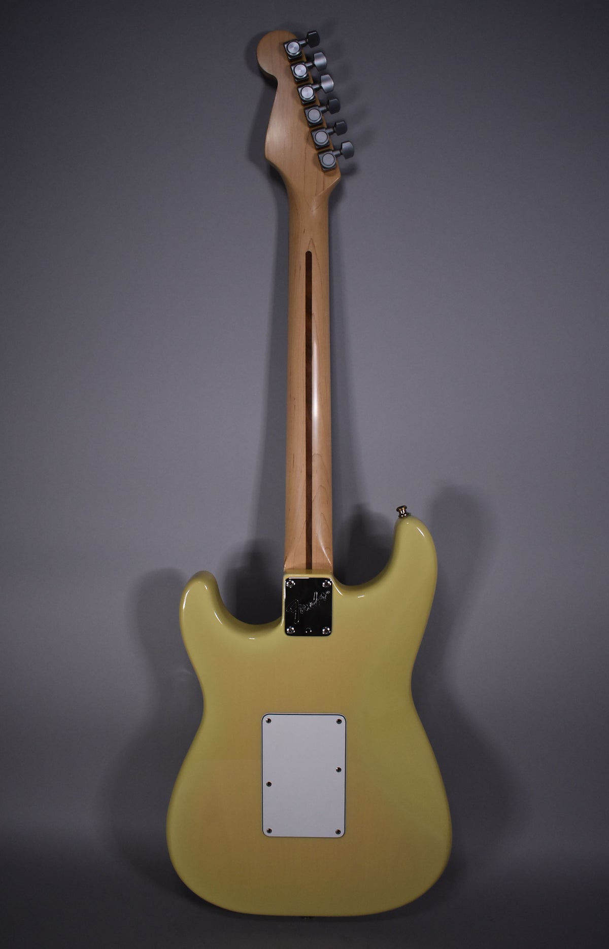 Full rear view of a vintage blonde Stratocaster with a maple neck, a white tremolo cover, and a chrome neck plate.