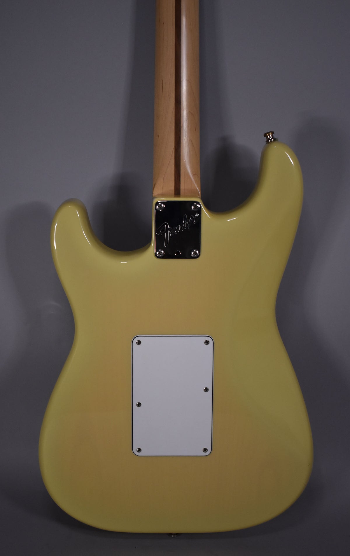 The back of a vintage blonde Stratocaster, showing the light maple neck, chrome neck plate, and white tremolo cover.