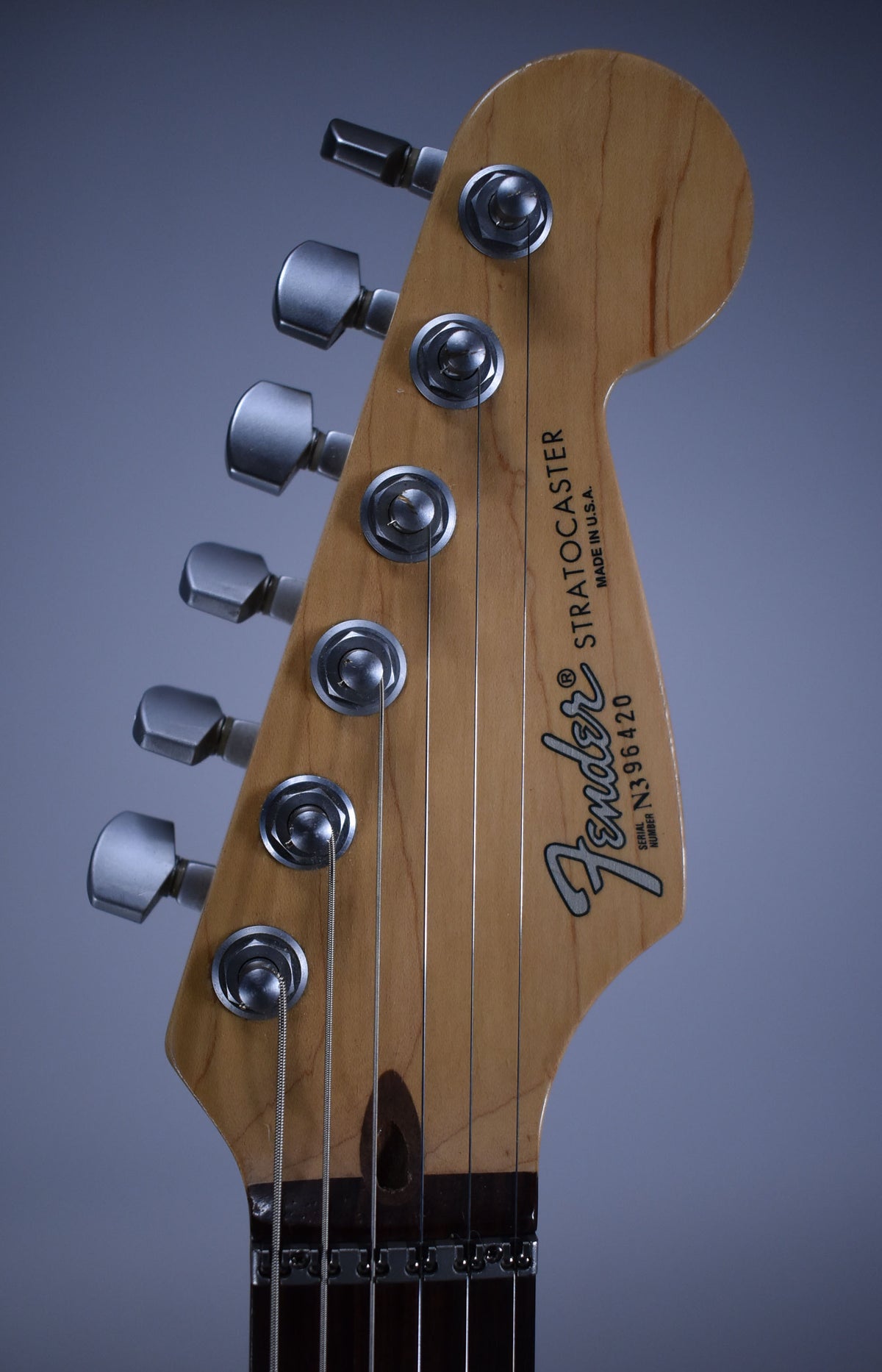 Close-up of the guitar's blonde headstock and tuning machines, showing the top three strings and a dark wood fretboard.