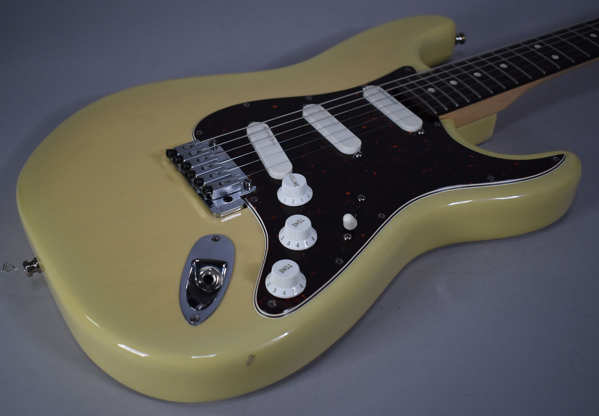 Angled view of a vintage blonde Stratocaster's body, showing a tortoiseshell pickguard, three white single-coil pickups, and chrome hardware.