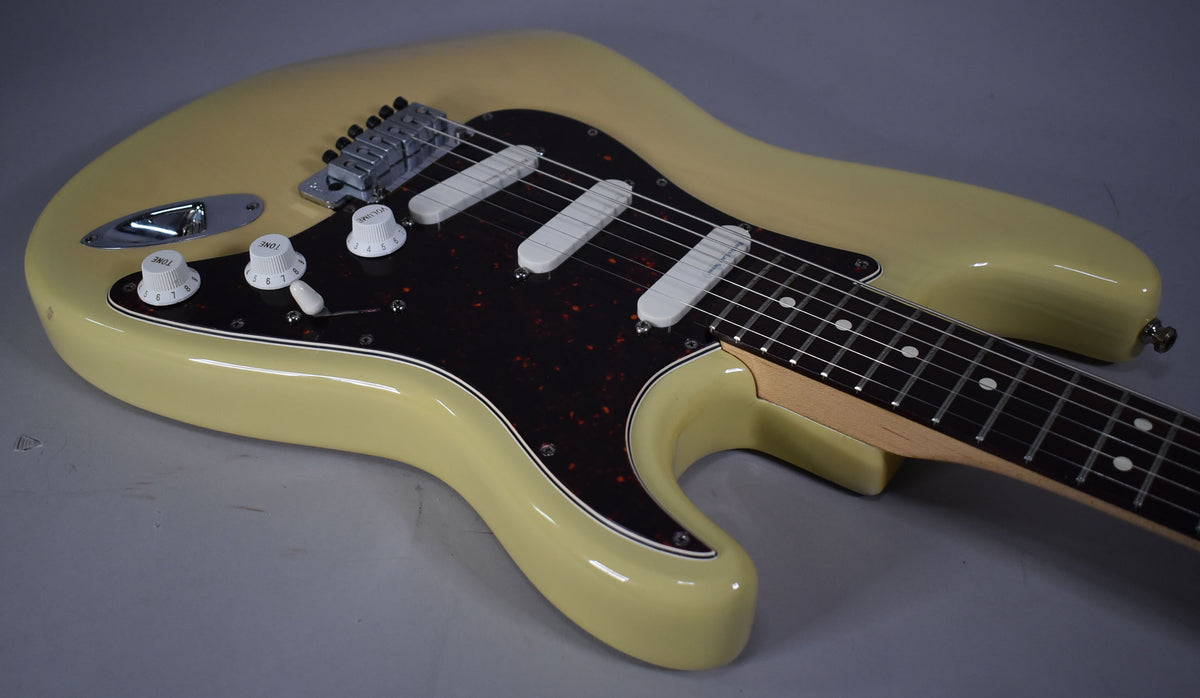 Blonde Stratocaster body, angled from the lower bout, showing the tortoiseshell pickguard, three white single-coil pickups, and controls.