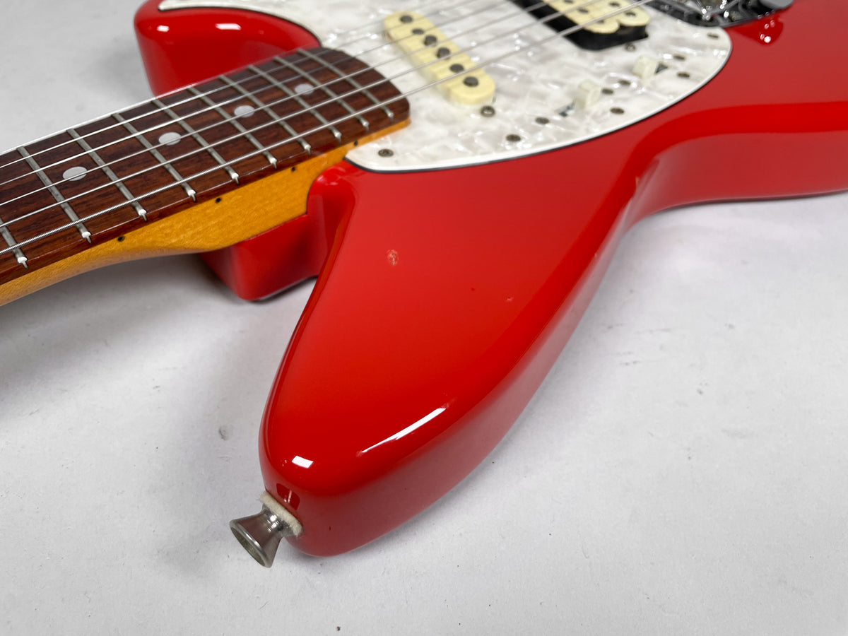 Close-up of the glossy red body, showing the neck joint, pearloid pickguard, cream pickups, and a small ding on the upper horn.
