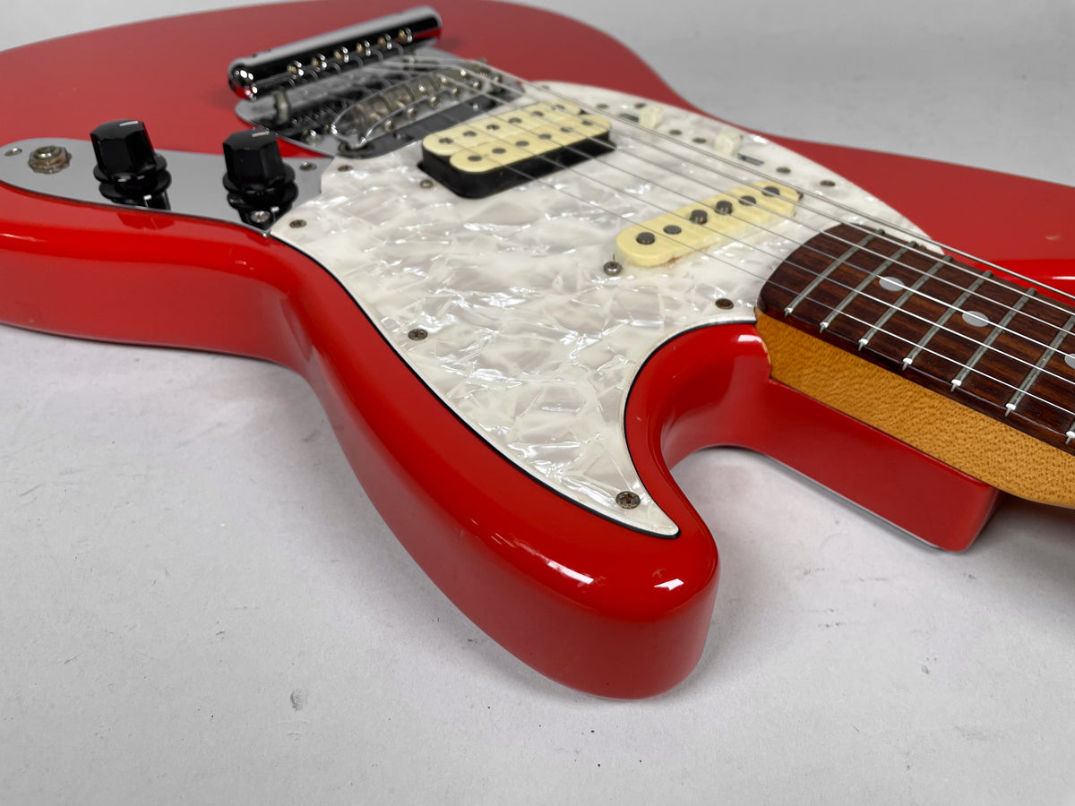 Close-up of a glossy red guitar body with a pearloid pickguard, two black control knobs, and a chrome bridge.