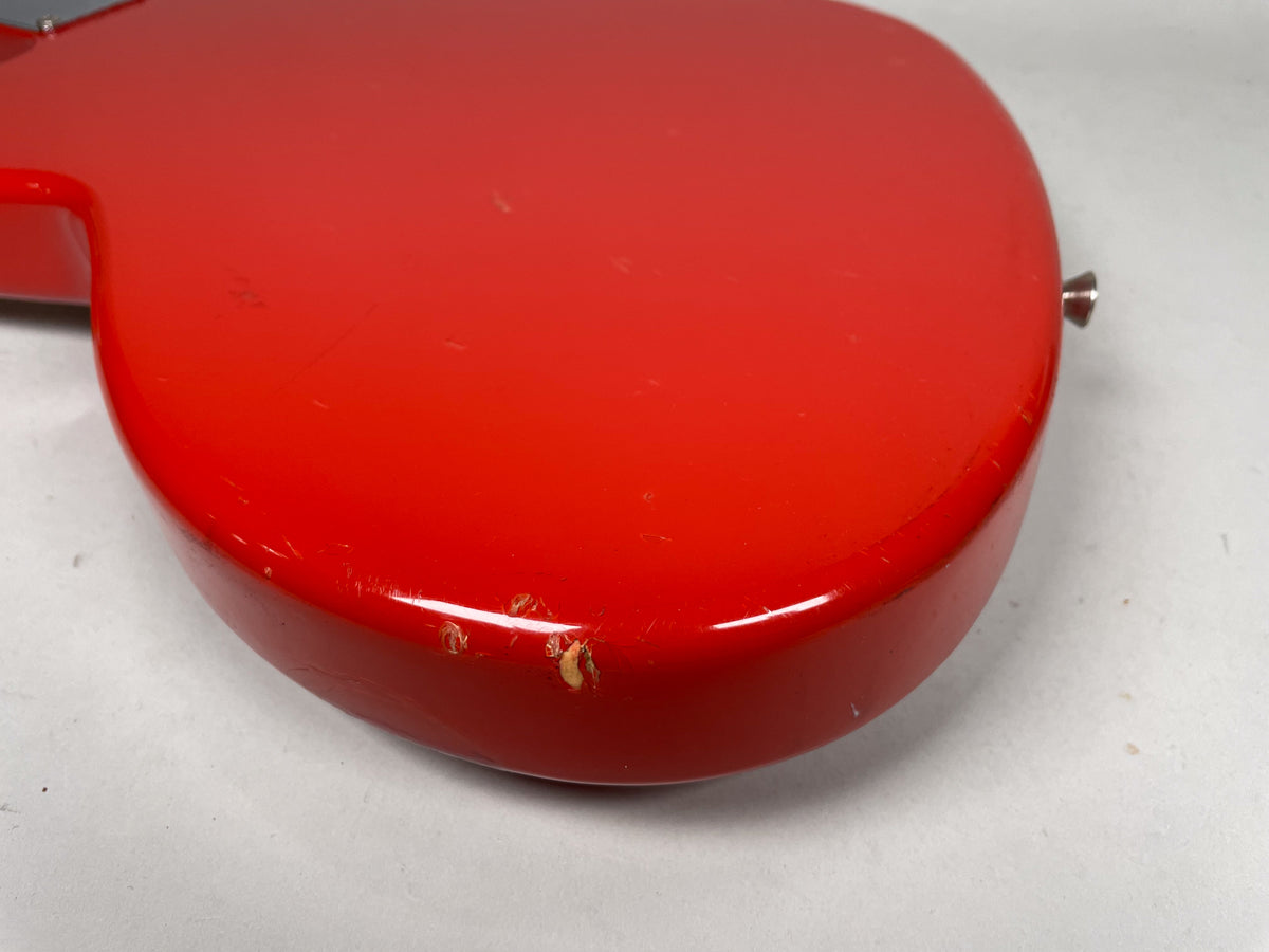 Close-up of the Fiesta Red guitar body's lower bout, showing several chips and scratches on the curved edge and flat surface.