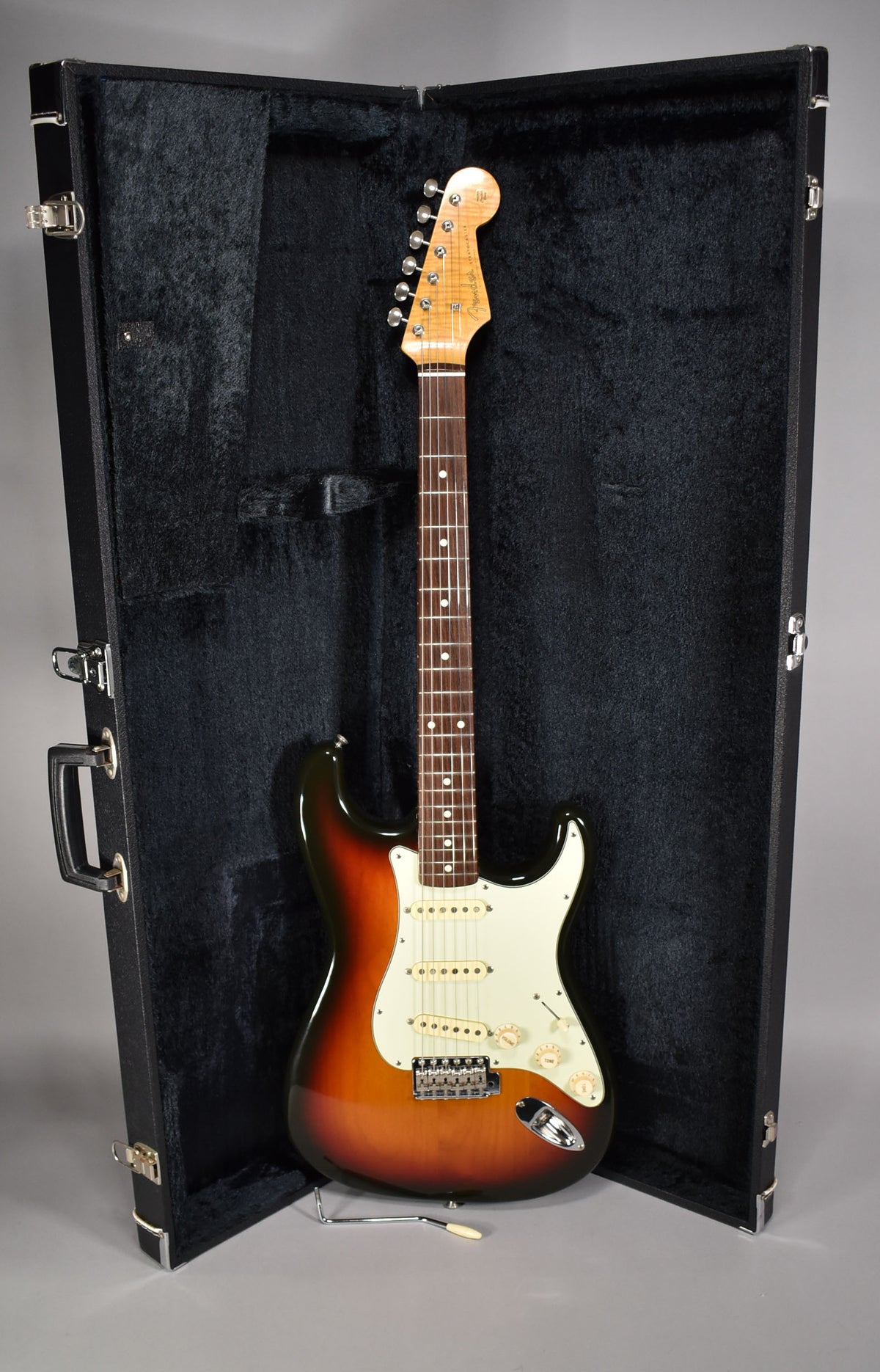 Full-length view of a sunburst electric guitar with a white pickguard and cream pickups, standing in an open black hard case.