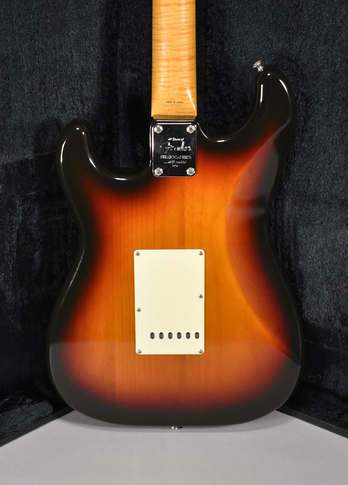 The guitar's back, in a glossy 3-tone sunburst, shows a light maple neck, chrome neck plate, and a cream tremolo cover.