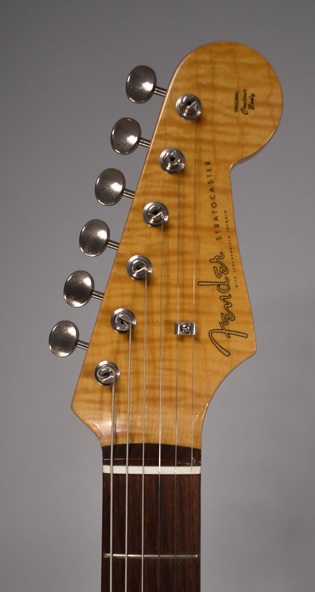 The guitar's headstock, with a flamed maple finish, six chrome tuners, and a dark rosewood fretboard, is shown from the front.