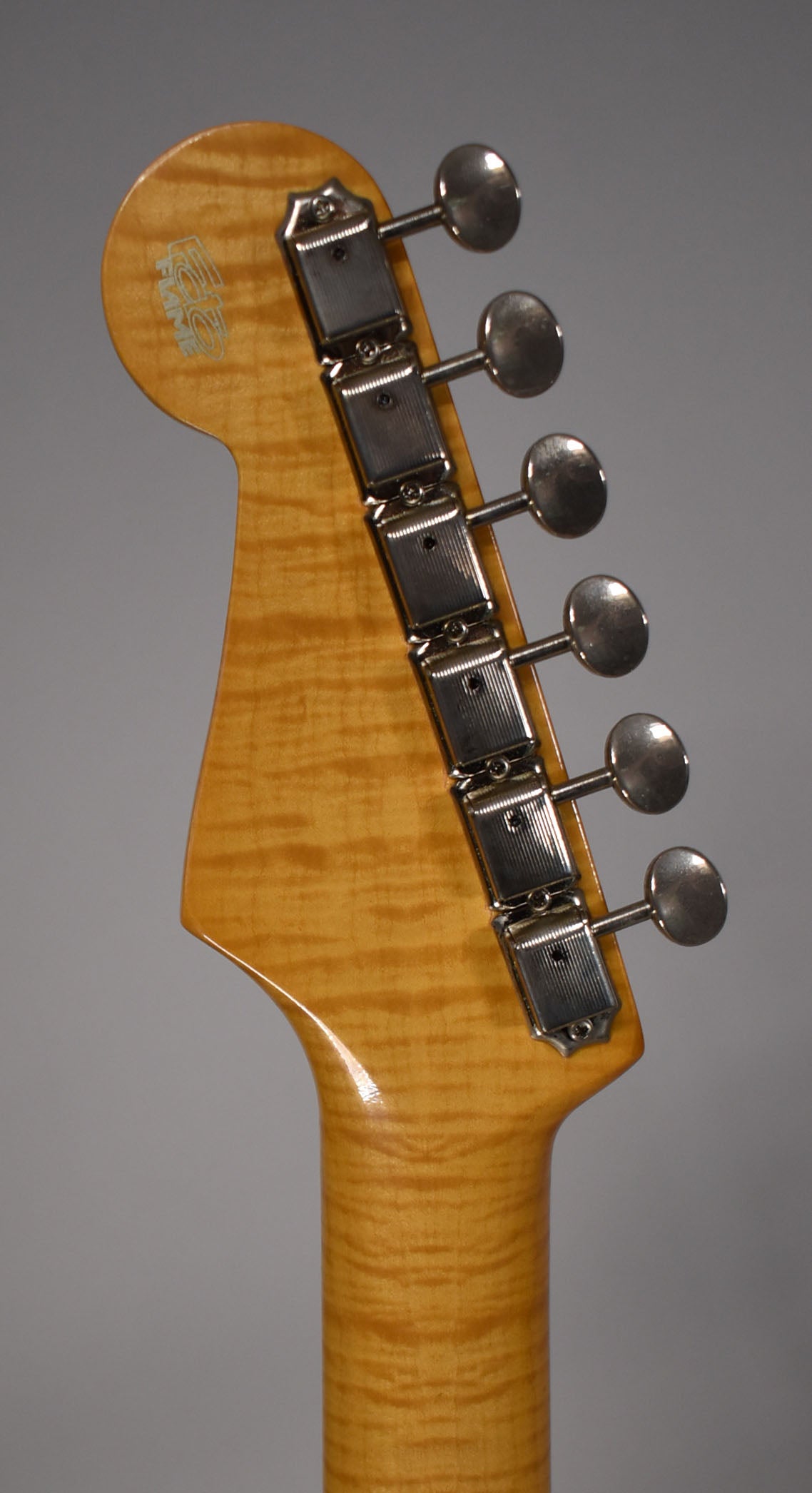 The guitar's headstock and upper neck are visible, showing a glossy amber finish with prominent flame maple figuring and six chrome tuners.