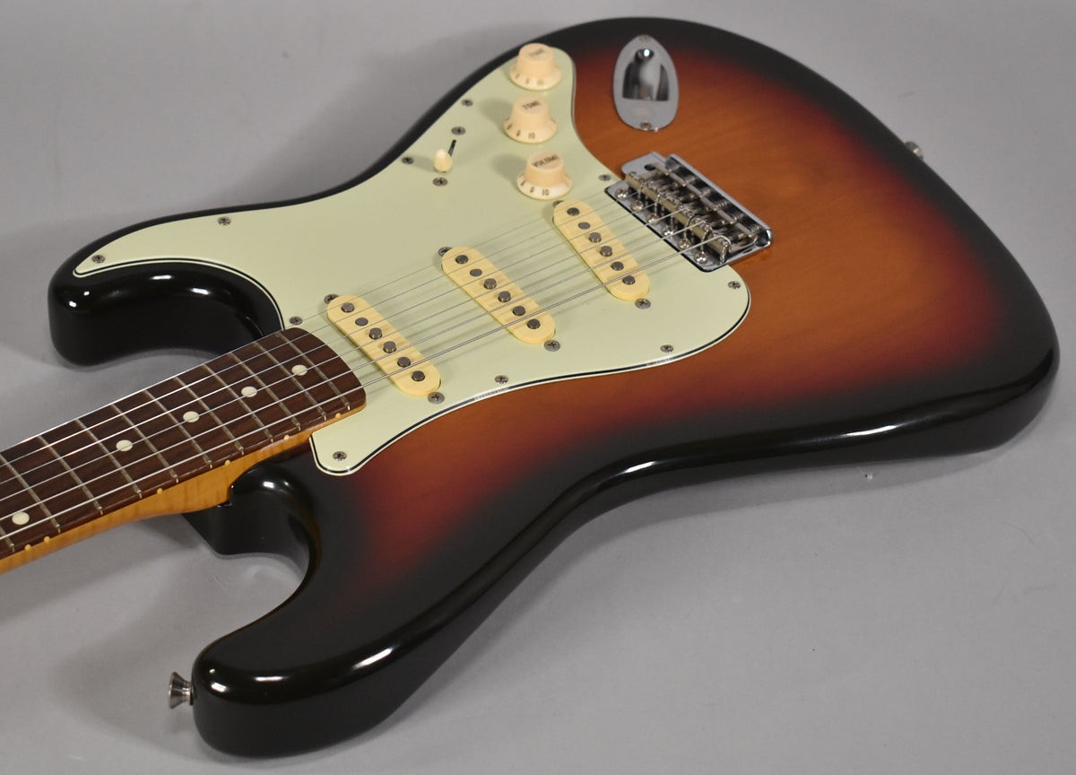 Sunburst Stratocaster body, angled from the lower left, showing the cream pickguard, three single-coil pickups, and chrome tremolo bridge.