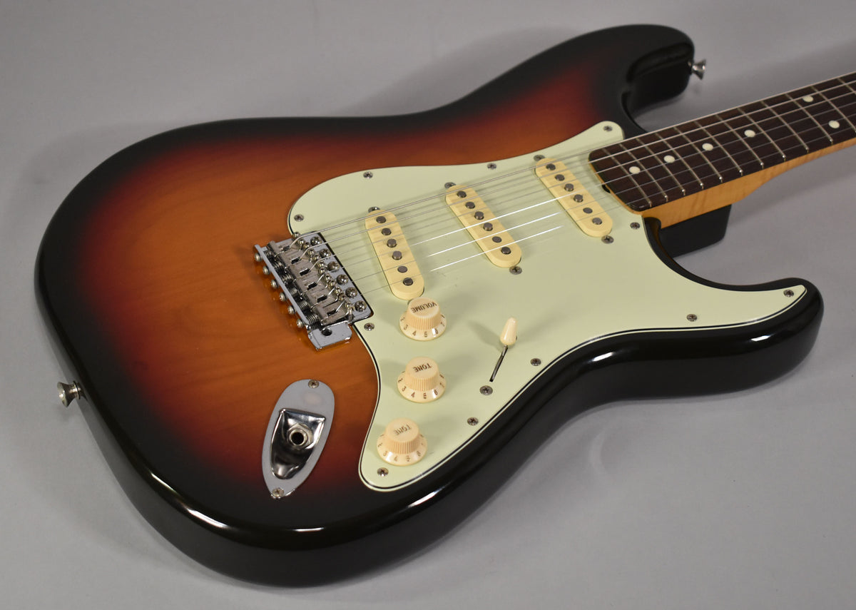 The sunburst Stratocaster body, with a mint green pickguard, cream pickups, and chrome hardware, is angled from the lower left.