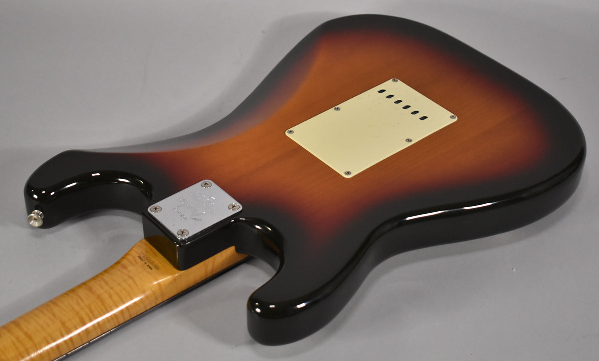 The guitar's back, a glossy 3-tone sunburst, shows a cream tremolo cover and a worn chrome neck plate on a maple neck.