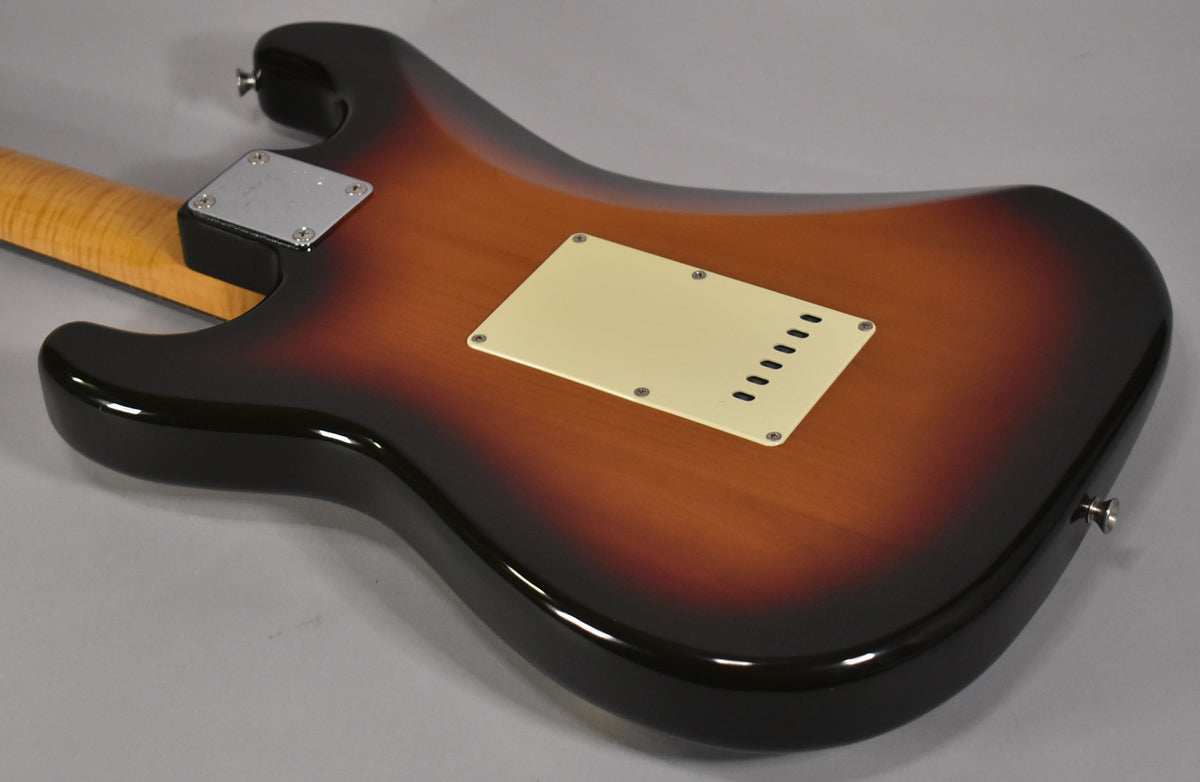 The guitar's sunburst body, viewed from the back, shows a cream tremolo cover and a chrome neck plate with light wear.