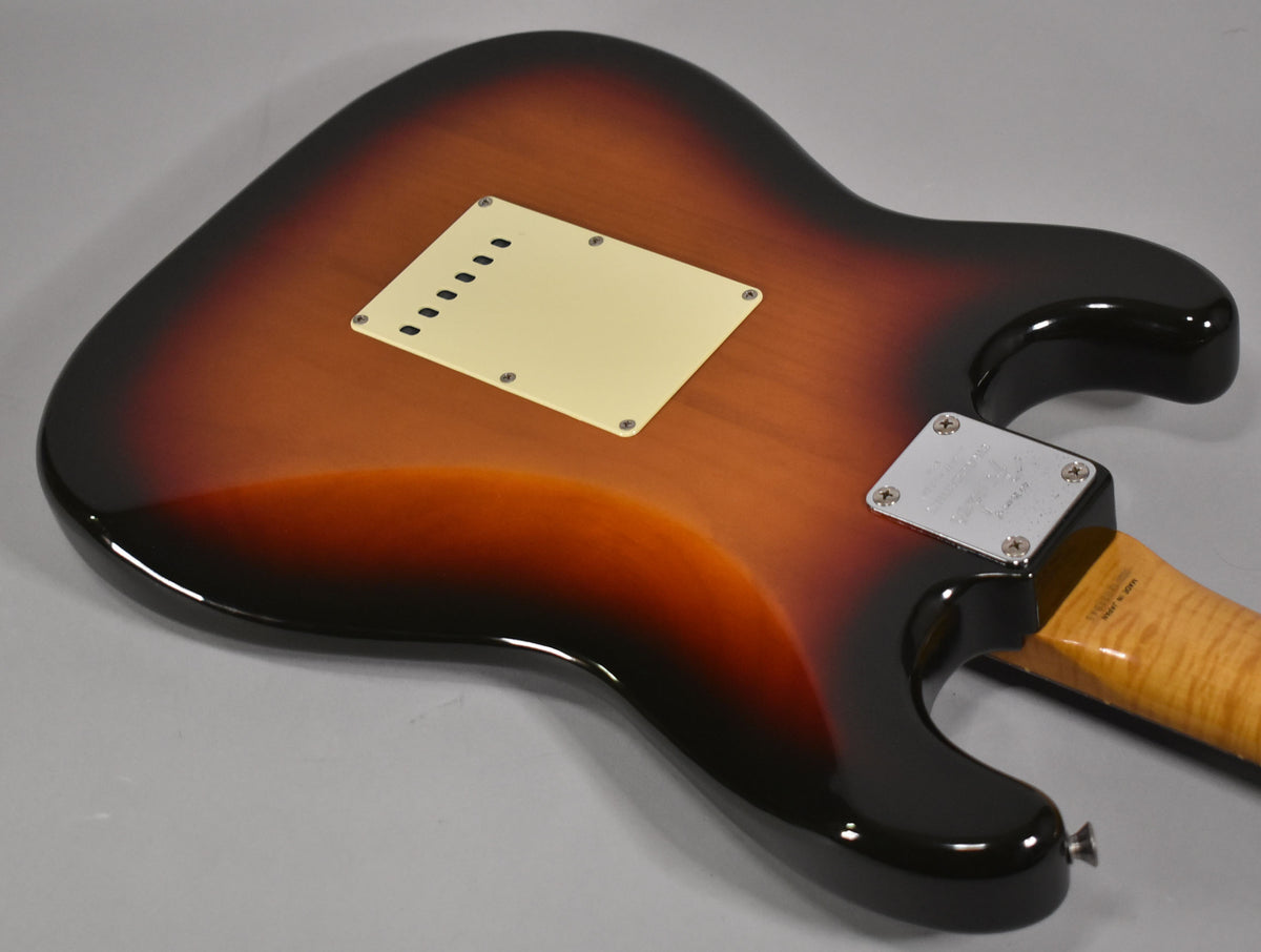 The guitar's sunburst body, with a cream tremolo cover and chrome neck plate, is viewed from the back at an angle.