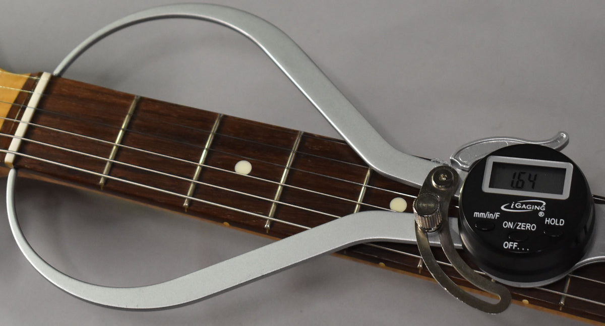 A digital caliper measures the guitar's dark rosewood fretboard, showing 1.64mm string height at the 7th fret.