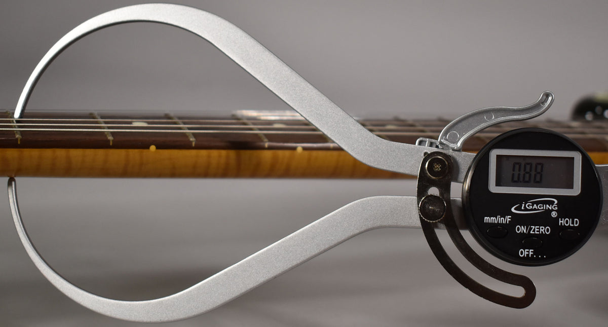 A digital caliper measures the guitar's fretboard and neck, showing a reading of 0.88, with a worn, amber-tinted maple neck.