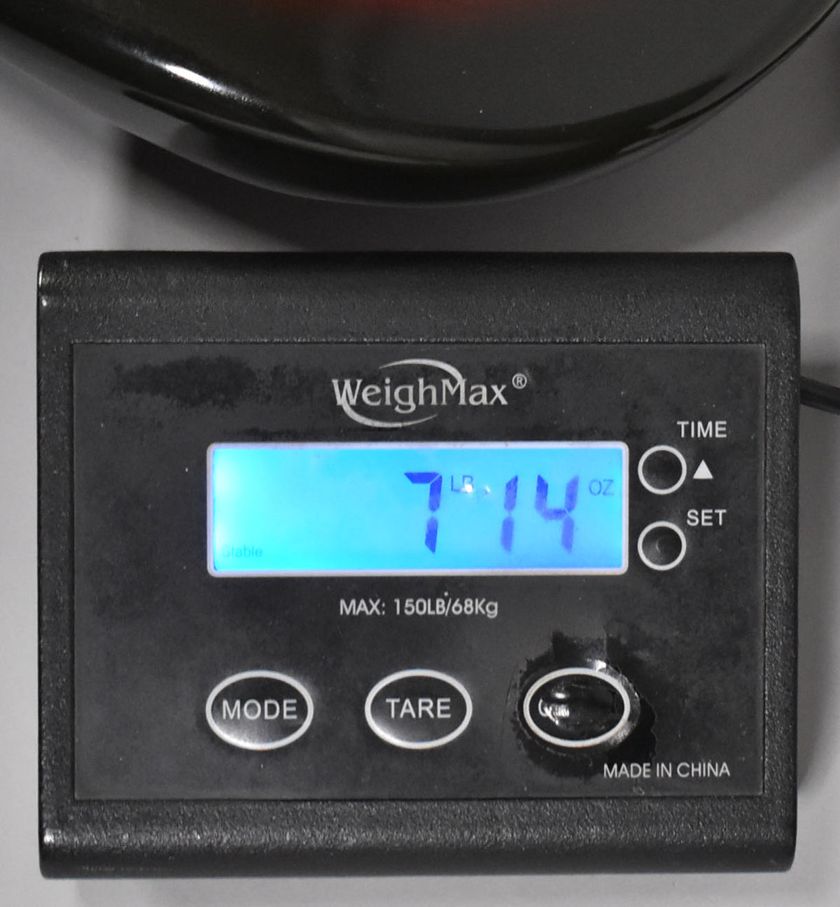 A black digital scale displays "7 LB 14 OZ" with a dark red guitar body partially visible above it.