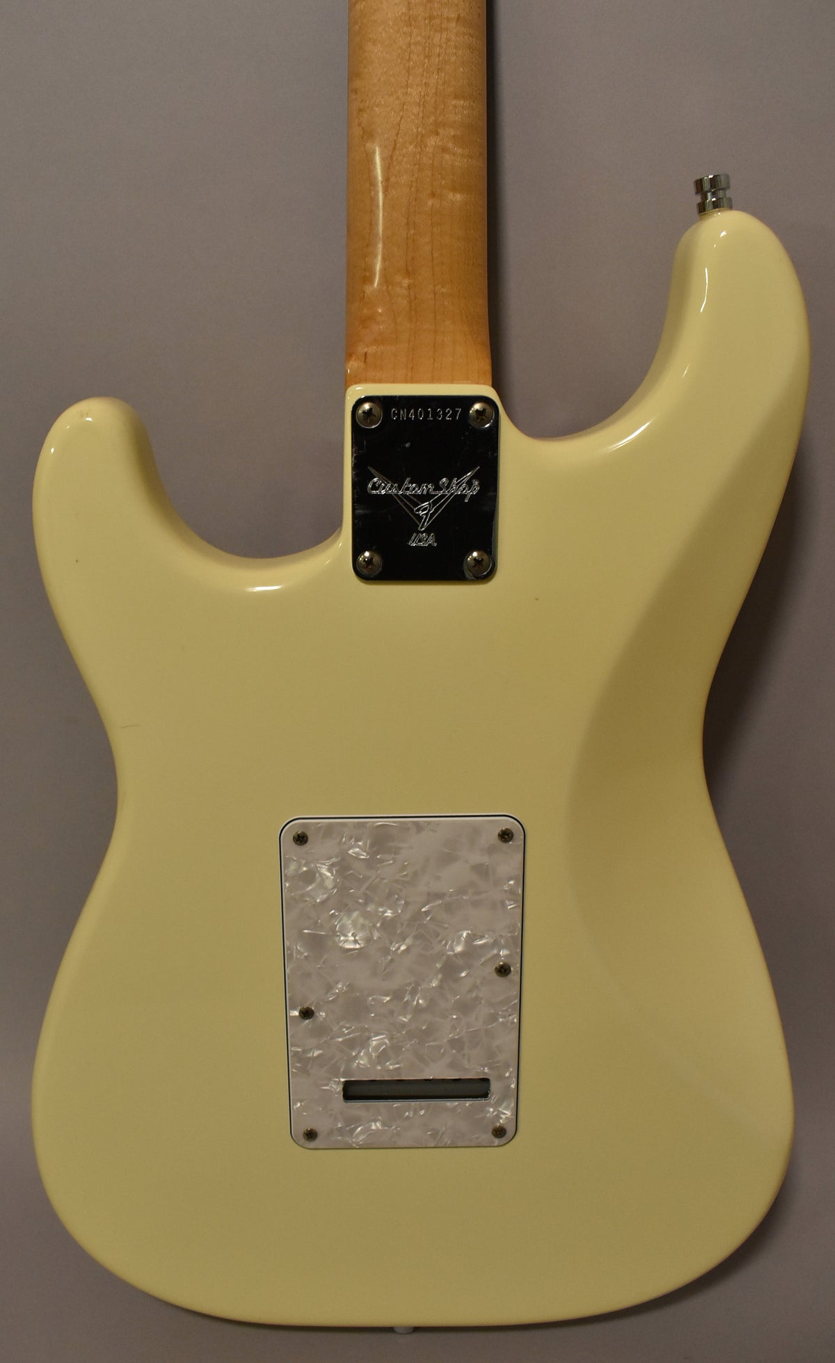 The back of an Olympic White Stratocaster with a pearloid tremolo cover and a light maple neck.