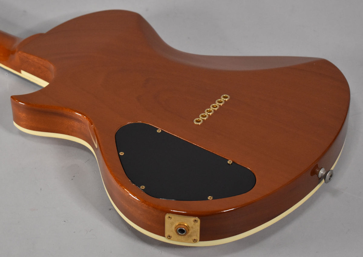The guitar's amber back shows a black control cavity cover, six gold string ferrules, and a gold output jack plate.