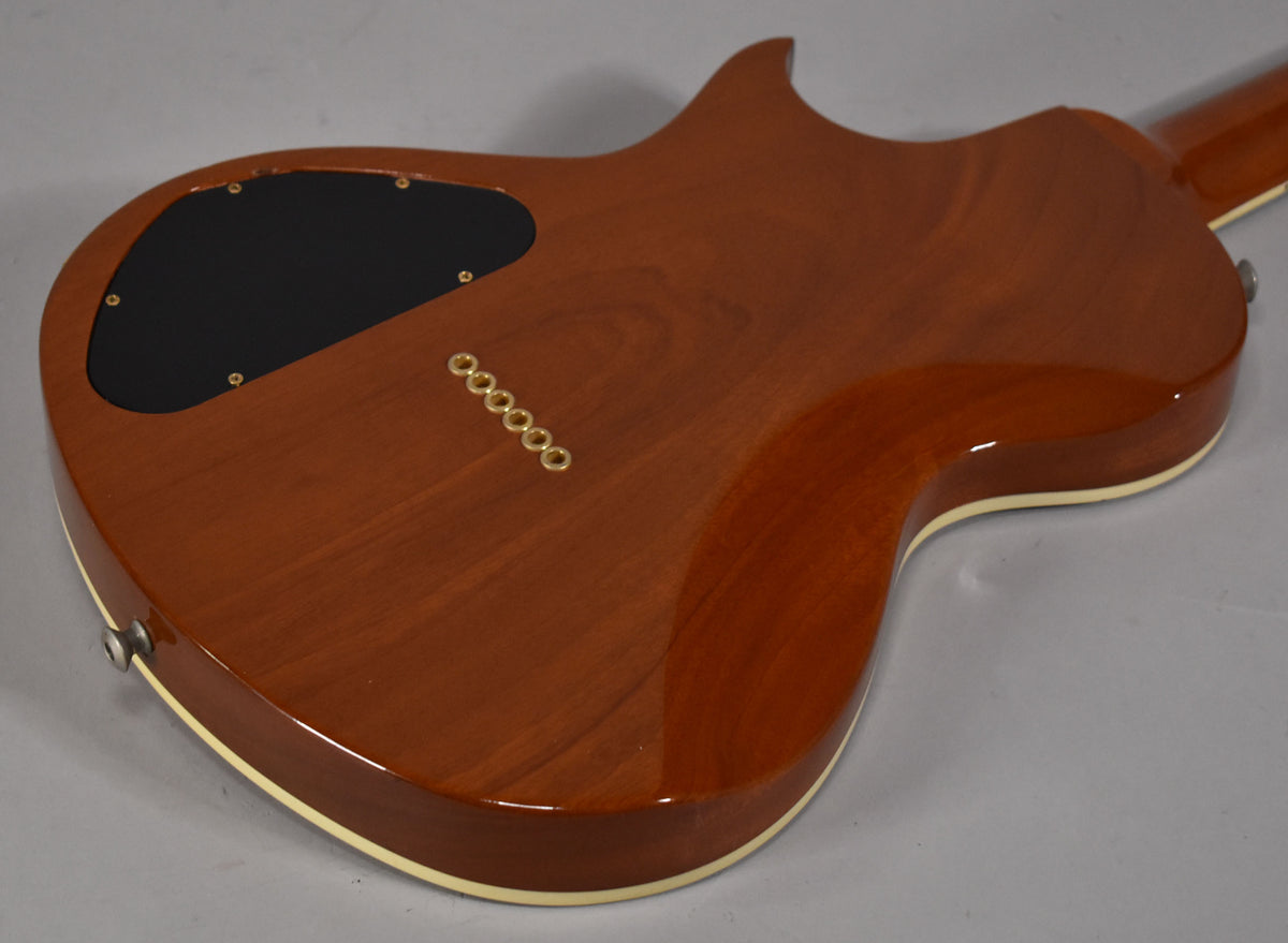 The guitar's amber-finished back shows a black control cavity cover, six gold string ferrules, and cream binding.
