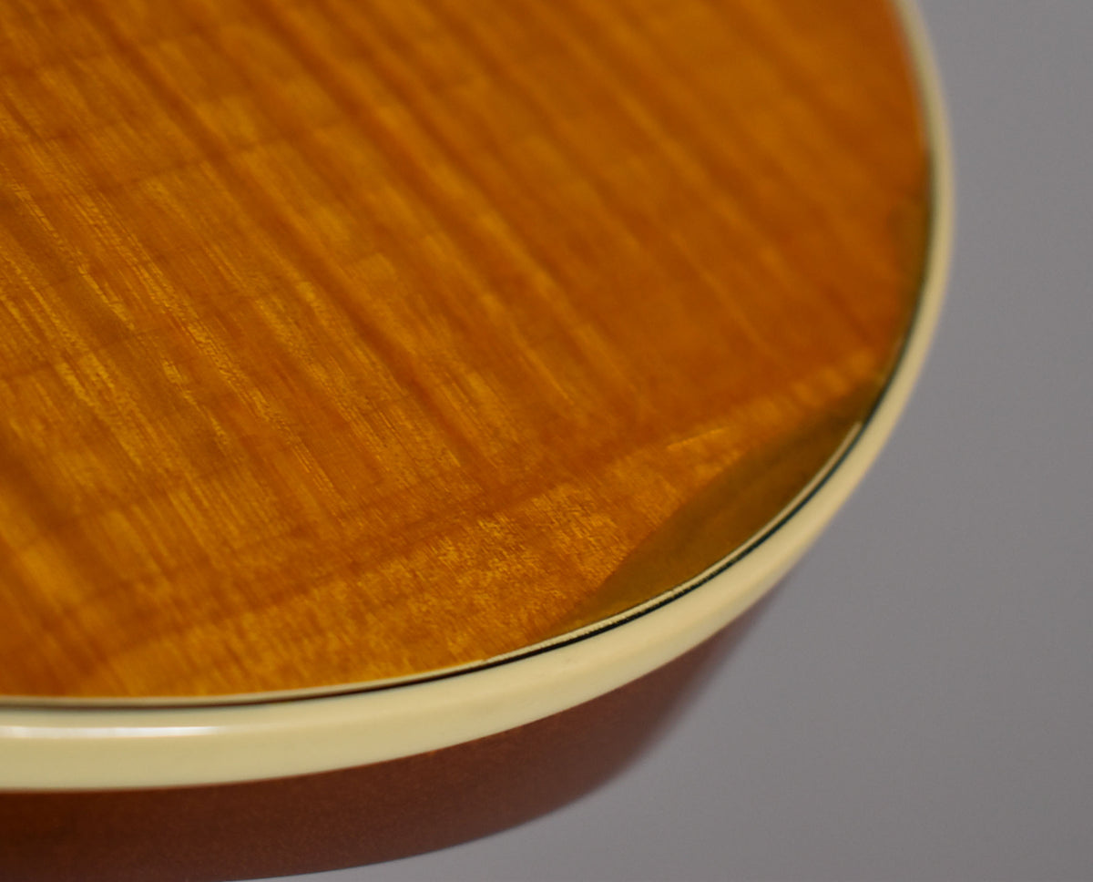 Close-up of the guitar's lower bout, showing the transparent amber finish with flame maple grain and cream binding with a thin black line.