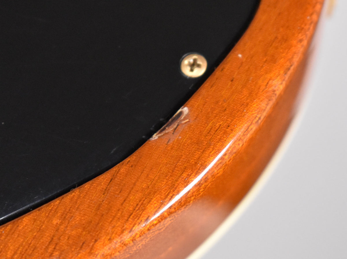 Close-up of the guitar's lower bout, showing a chip in the transparent amber finish near a black control cavity cover and gold screw.