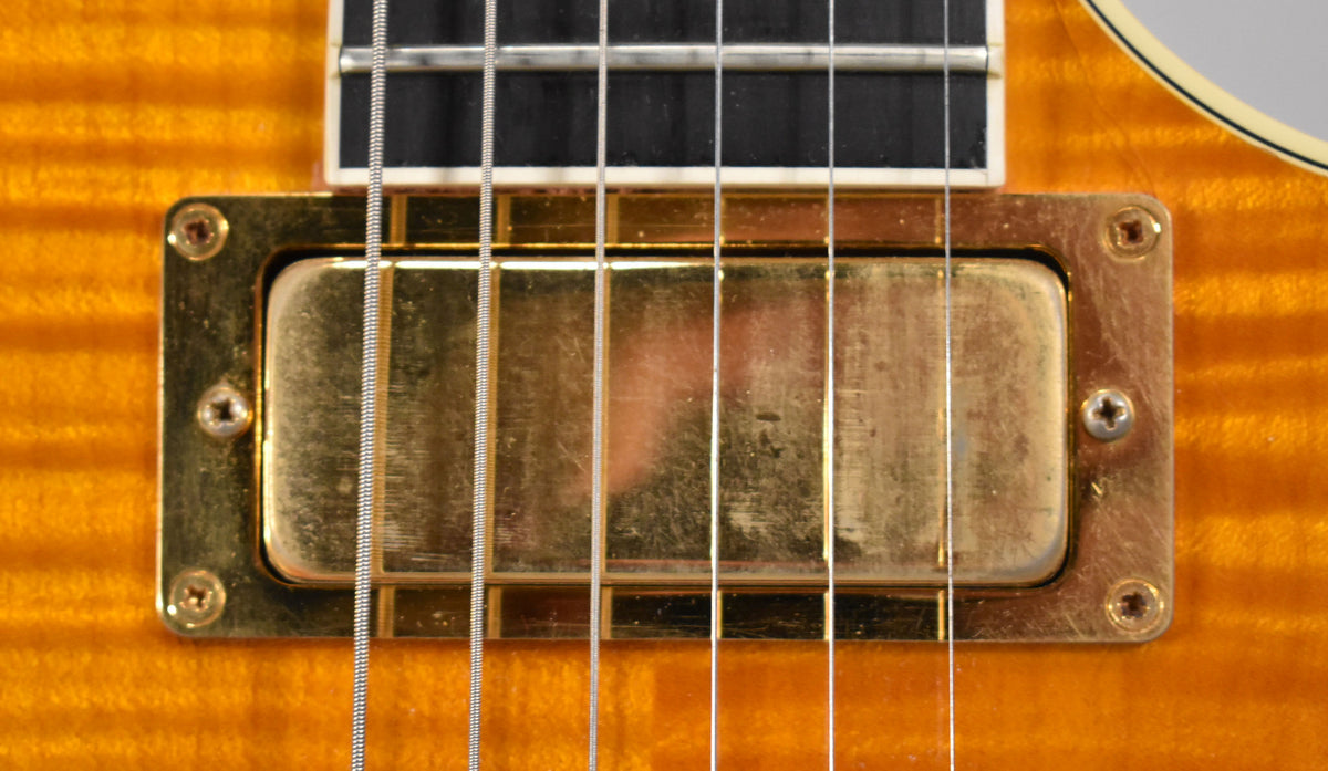 Close-up of the guitar's amber flamed maple body and gold humbucker pickup, showing light scratches and wear on the hardware.
