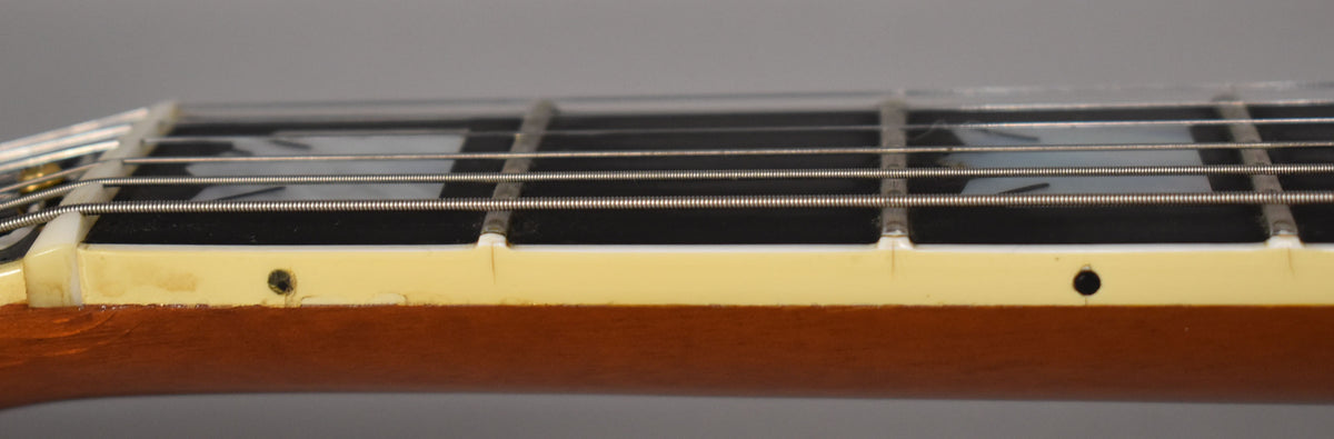 Close-up of the guitar's fretboard, showing cream binding with two side dots, some wear, and a crack near the nut.