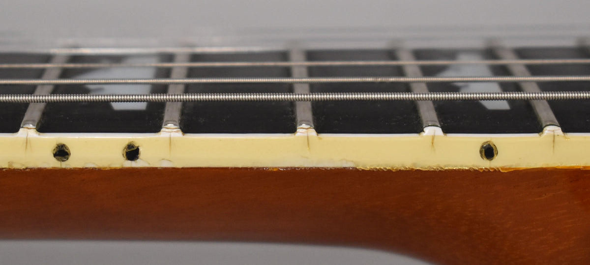 Close-up of the guitar's fretboard binding, showing wear, cracks, and three black side dot markers on the aged cream binding.