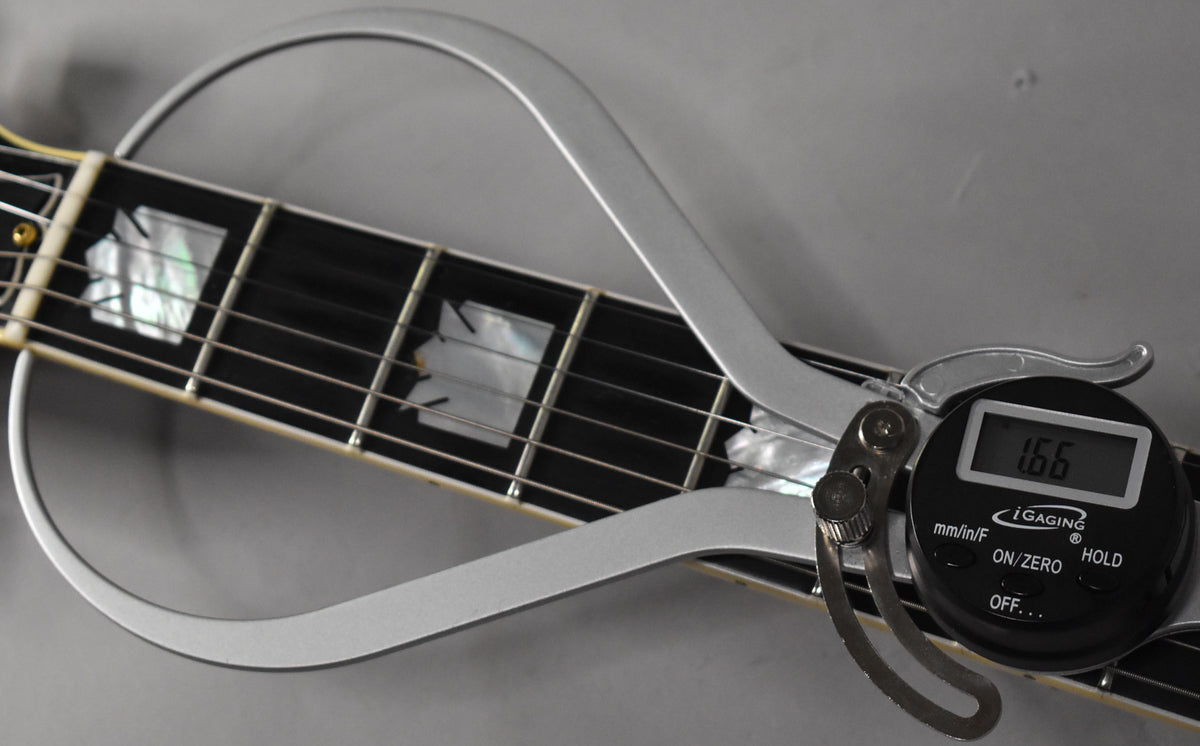 A close-up of the guitar's fretboard with block inlays, showing a digital string action gauge measuring 1.66mm at the 12th fret.