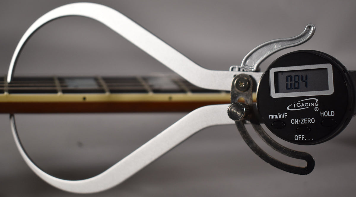 A digital caliper measures the guitar's neck relief at 0.04 inches, showing the fretboard and frets in soft focus.