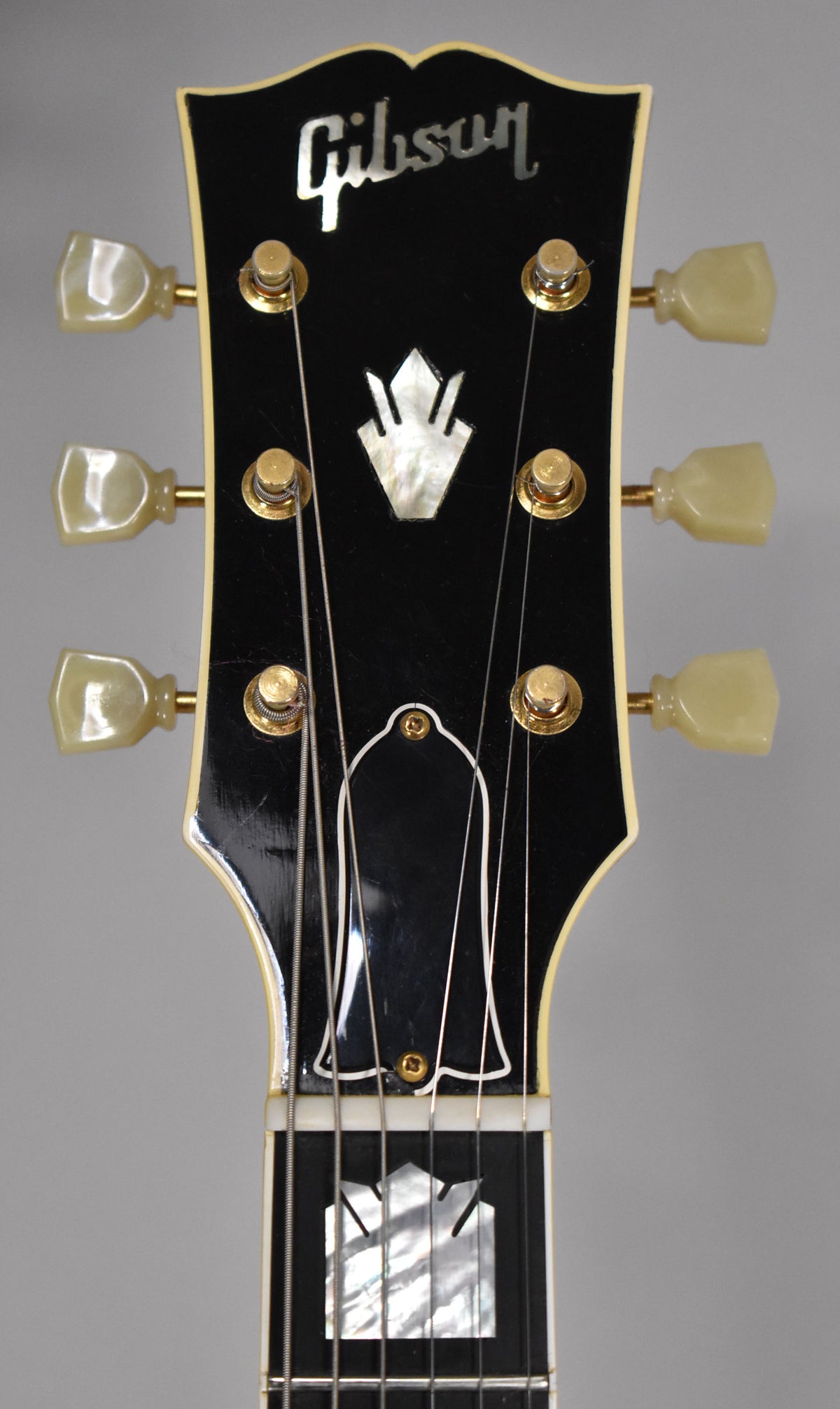 Close-up of the black headstock with cream binding, showing gold tuners with cream buttons and a mother-of-pearl crown inlay.