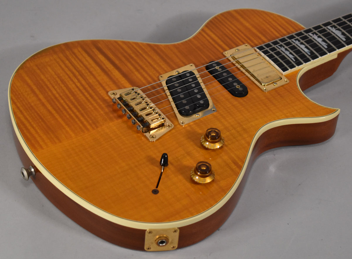 Close-up of the transparent amber flamed maple top, showing gold hardware, two black humbuckers, and two amber control knobs.