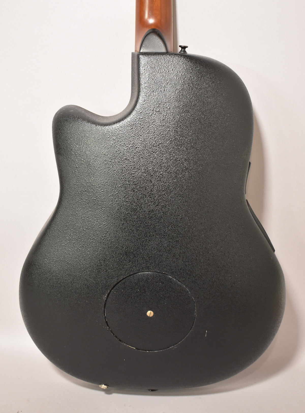 The guitar's textured black back is shown, with a circular access panel and a small gold screw near the bottom.