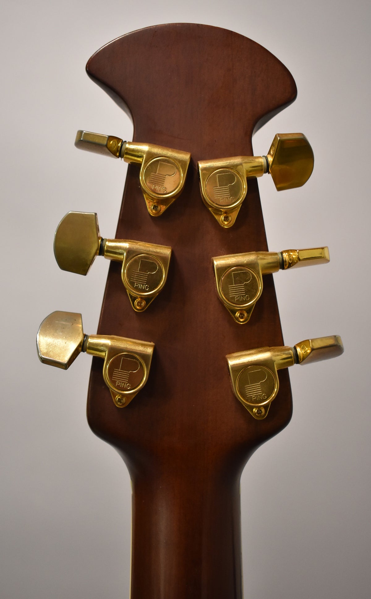 The back of a dark brown headstock with six gold tuning machines, showing some light wear and tarnishing.